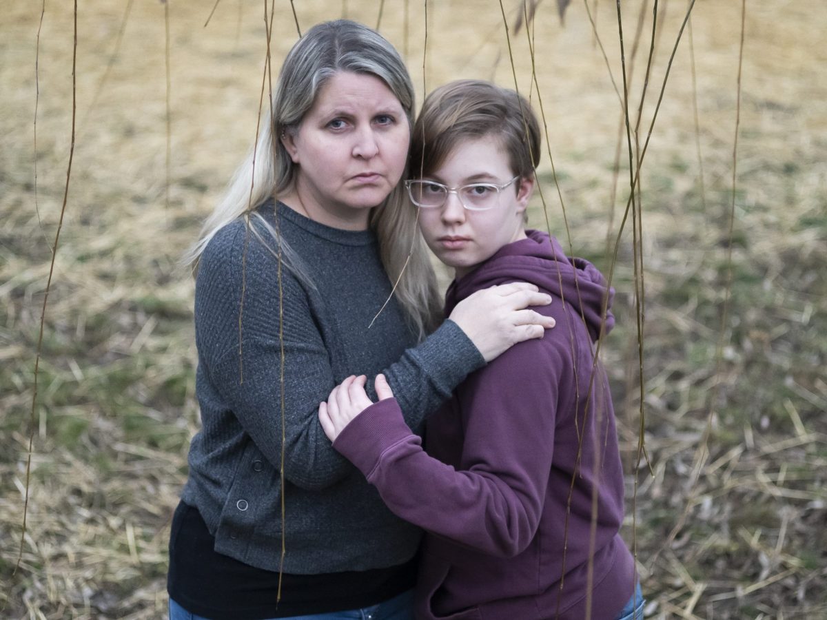 Lisa Norris stands hugging her daughter Hannah. Lisa has long blond hair and is wearing a blue sweater. Hanna has short brown hair and wears glasses and a purple hoodie.