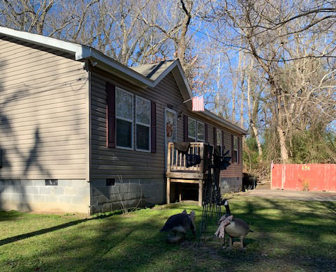 A sideview of Betty Ricks' home. It is one level, light brown with burgandy shutters. Two geese are in front of the home.