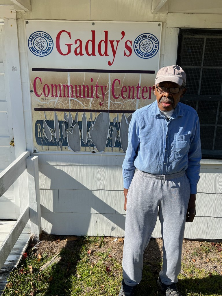 David H. Gaddy Jr., stands in from of Gaddy's Community Center. He wears glasses, a blue buttong-down shirt and sweatpants. 
