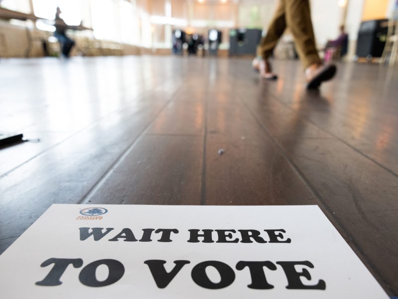 A "wait here to vote" sign lies on the floor as a person walks by it.