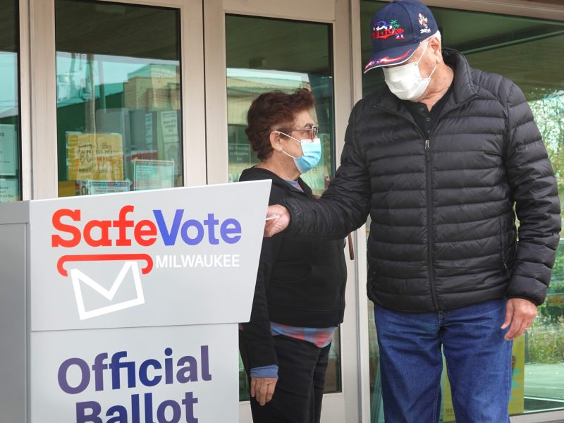 A voter wearing a mask puts a ballot into an election drop box.