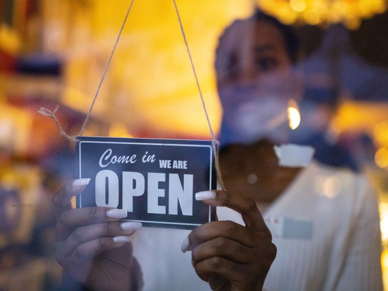 Woman turning an open sign on glass front door of coffee shop.