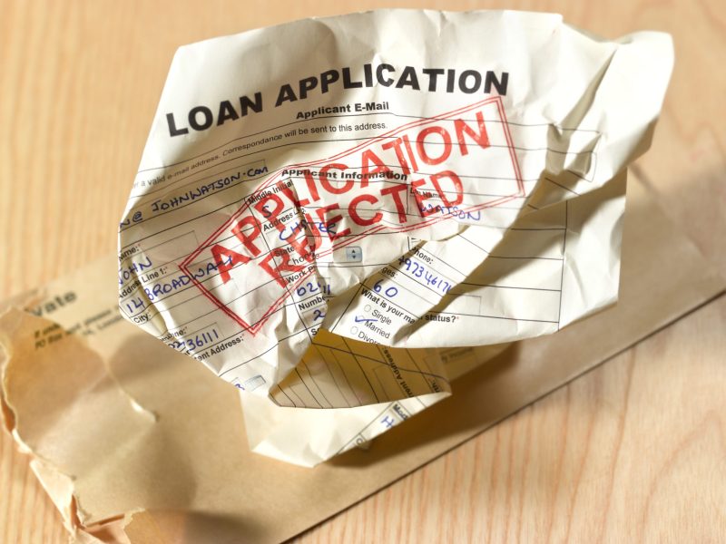 A bank loan application is crumbled. It has application rejected stamped on it.