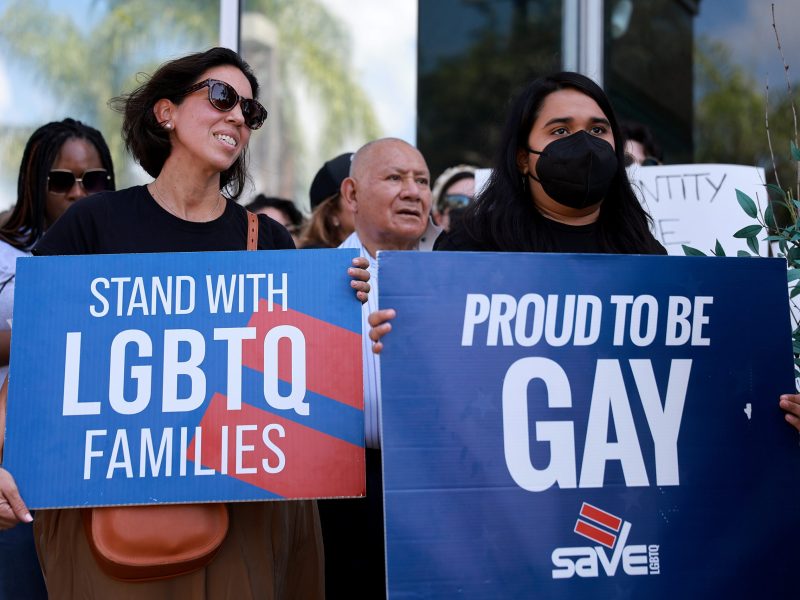 A protestor holds a sign that reads "Standing with LGBTQ families" while another protestor holds a sign that reads "Proud to be Gay" in opposition to the 'Don't Say Gay' bill