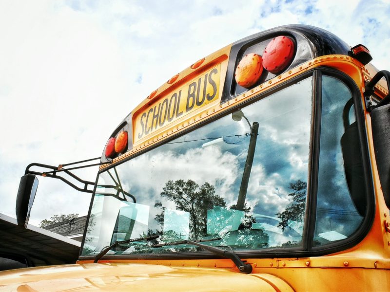 A yellow school bus up close to the camera, with a slightly clouded blue sky visible behind it.