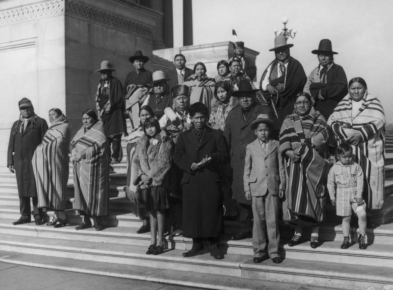 About two dozen adults and children stand on the steps of the Capitol Building in a black and white photo, their expressions somber.