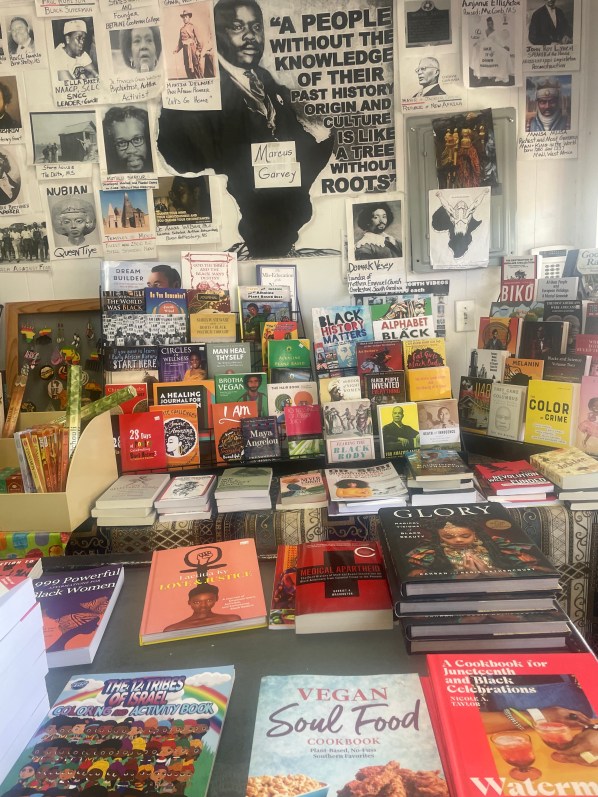 This image from inside the shop shows many books (including Vegan Soul Food, Black History Matters and Dream Builder) and a wall covered with images and posters, including a quote from Marcus Garvey: "A people without the knowledge of their past history, origin and culture is like a tree without roots."
