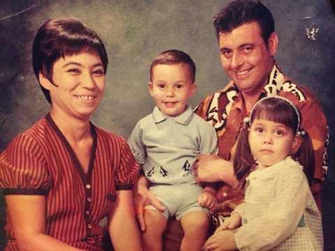 A family portrait of the Carson family from 1971. Joaquin's mother is on the left. She has short dark hair and is wearing a short-sleeved shirt with red and black strips.  Joaquin is in the middle. He is smiling and wearing a light blue shirt with penguins along the bottom. On the right is Joaquin's father. He is wearing a brown and white patterned shirt. He has short dark hair and is smiling. He is holding Joaquin's left arm. In front of Joaquin's dad is Diana.  She has her dark hair in pigtails and wears a headband. She is wearing a white top and is not smiling.