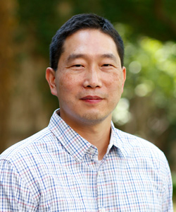 Michael Kang poses in a plaid shirt button-down shirt. 