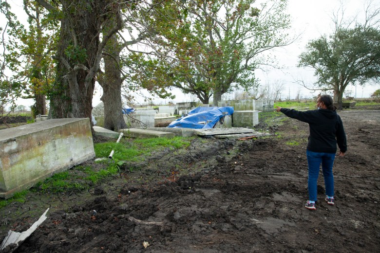 Cassandra Wilson, dressed in a sweatshirt, jeans and sneakers, points to caskets that have surfaced above ground after a hurricane.